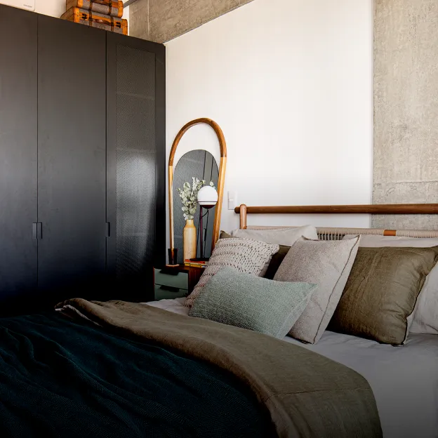 Um quarto acolhedor com guarda-roupa escuro, espelho oval e cama com almofadas verdes e bege.