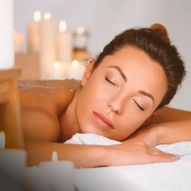 Uma mulher relaxando de olhos fechados durante um tratamento de spa, rodeada por velas acesas.