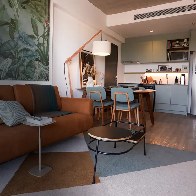 Uma sala de estar e cozinha mobiliadas, com sofá marrom, mesa de jantar e geladeira em inox.